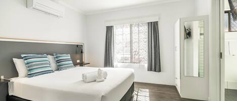 Une chambre d’hôtel moderne avec un grand lit, une table de chevet, une fenêtre avec des rideaux et un appareil de climatisation.
