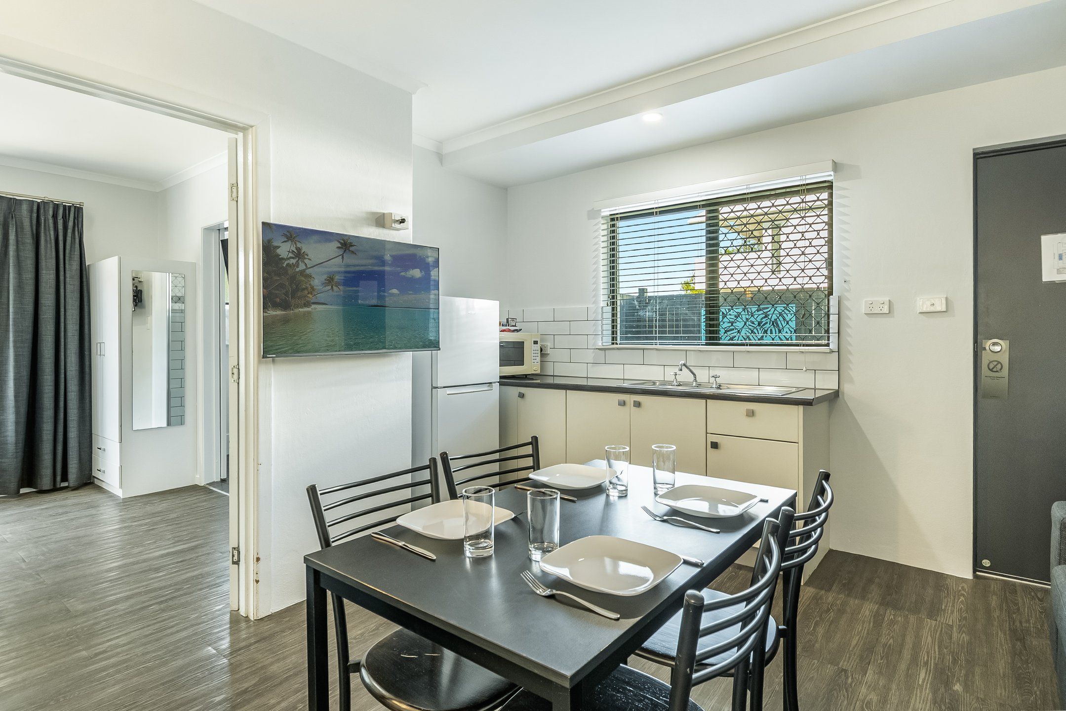 Cocina compacta con comedor, refrigerador, microondas y ventana con persianas.