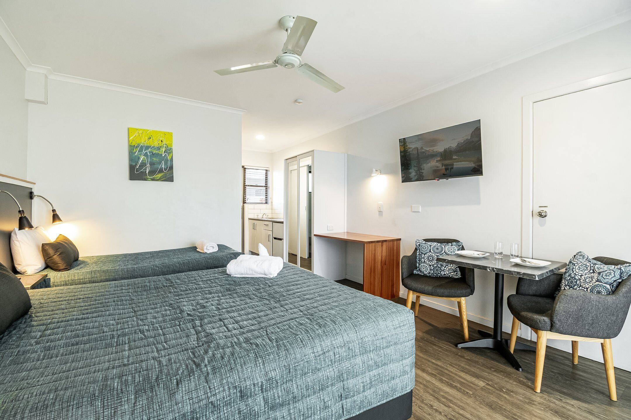 A hotel room with a bed, a desk, a chair, a ceiling fan, and a TV on the wall.