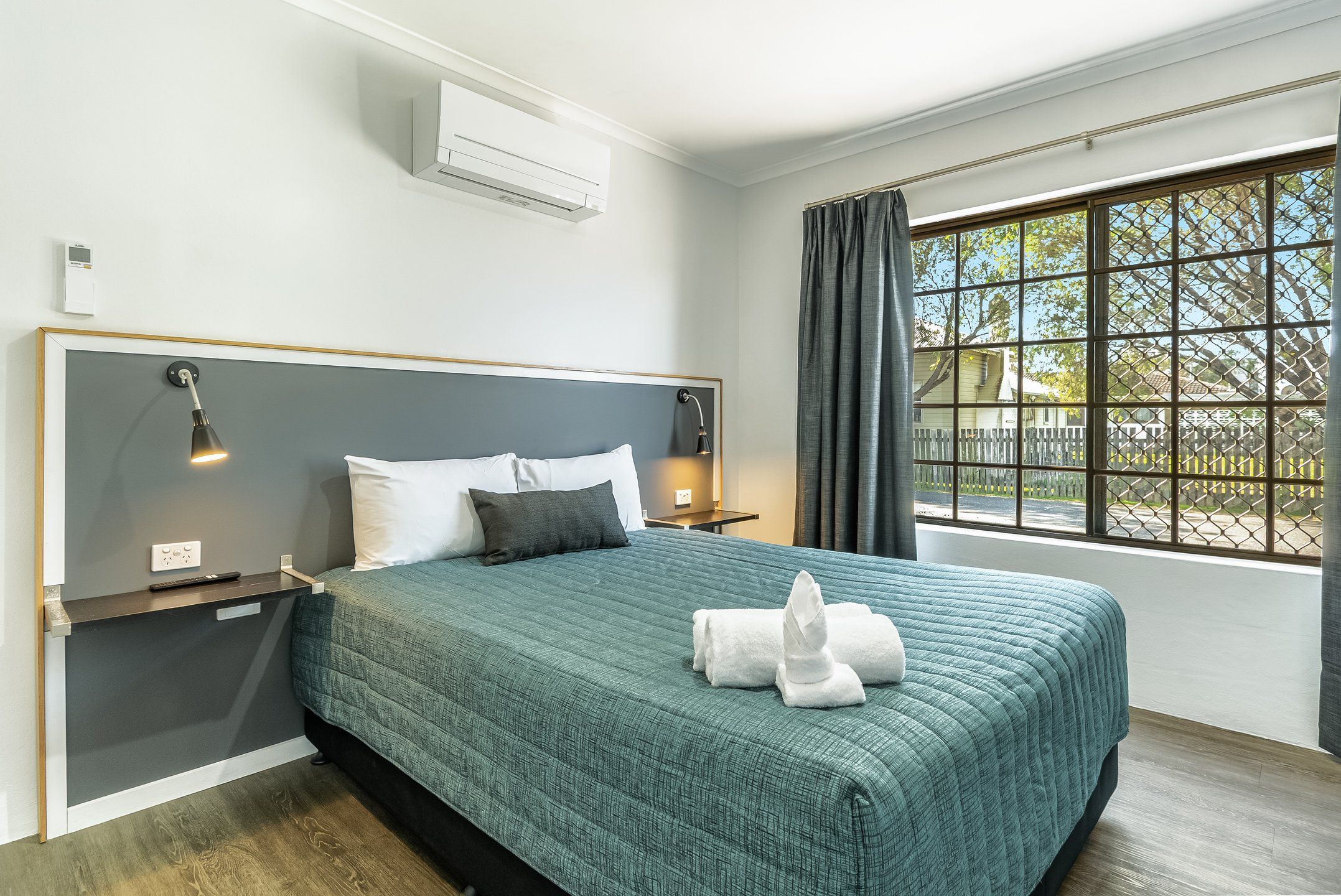 A modern hotel room with a large bed, bedside lamps, a window with a view, and a built-in air conditioning unit.