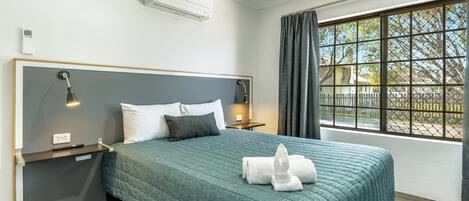Moderni hotellihuone, jossa on suuri sänky, yöpöytävalaisimet, ikkuna, josta on näkymä, ja sisäänrakennettu ilmastointilaite.