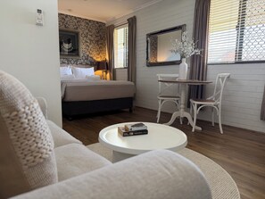 A bedroom with a bed, bedside table, lamp, and a mirror. There is a white chair and a small table with books. - Ballina Travellers Lodge (Ballina)