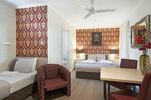Une chambre d’hôtel comprenant un lit, deux tables de chevet, un bureau, une chaise, un ventilateur de plafond et un papier peint à motifs.