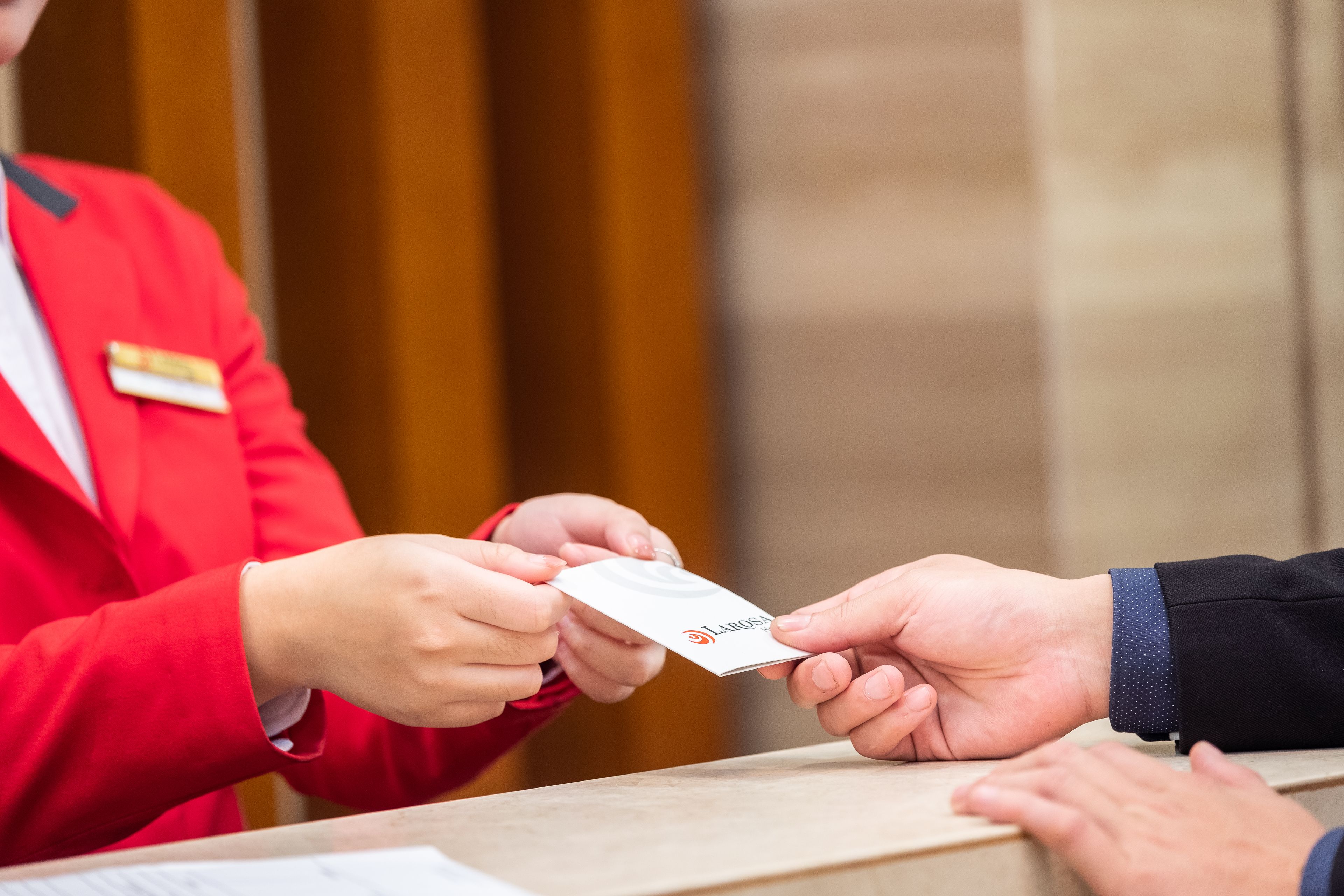 A person in a red uniform handing over a card to another person at a reception desk.