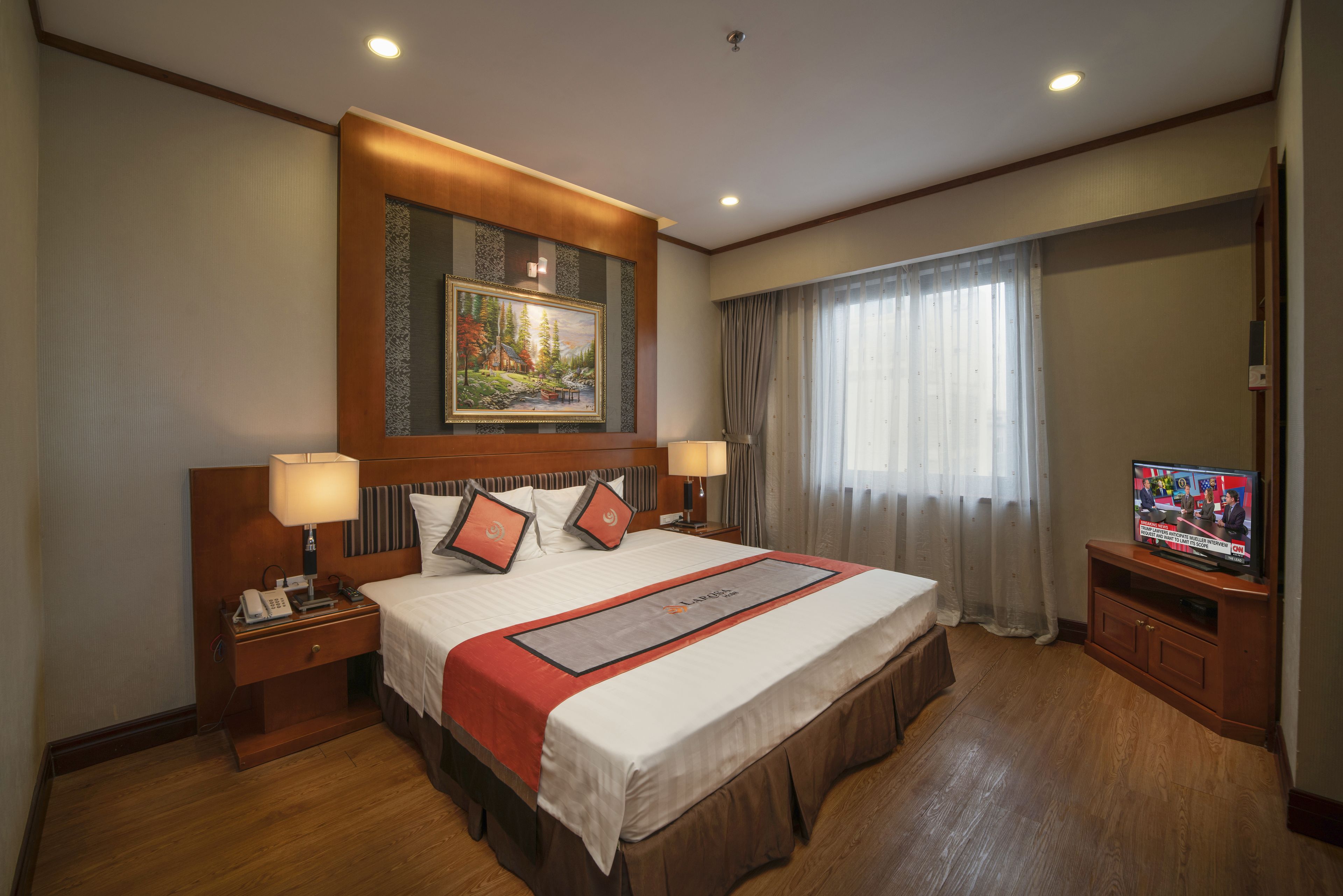 A hotel room with a large bed, a television, a painting, and a wooden floor.
