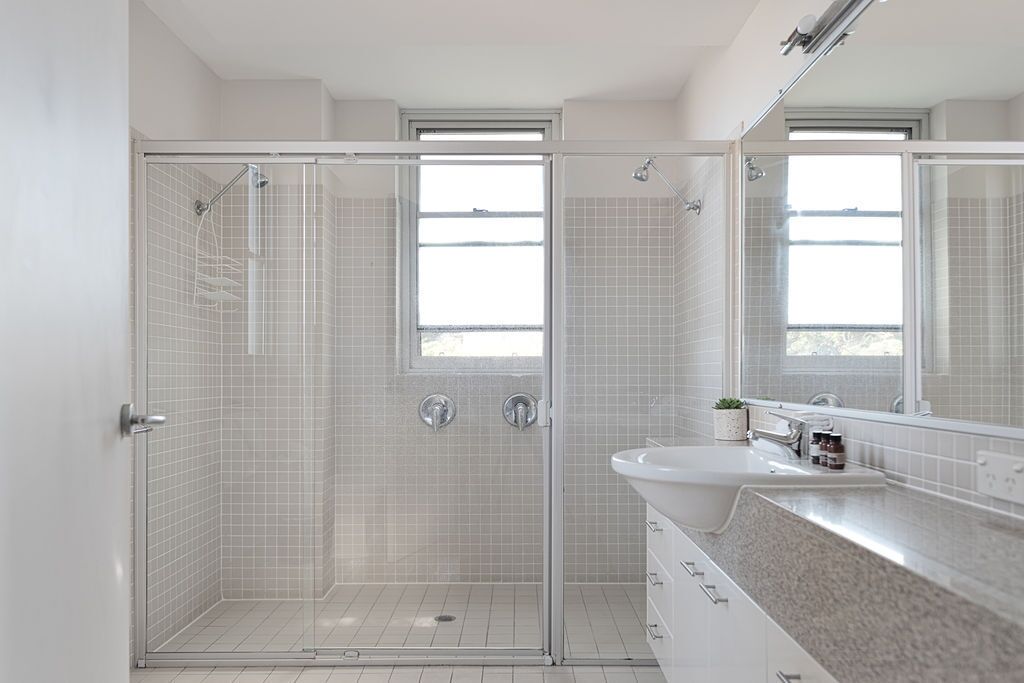 Un baño moderno con ducha envuelta en vidrio, un lavamanos con espejo y una ventana que proporciona luz natural.