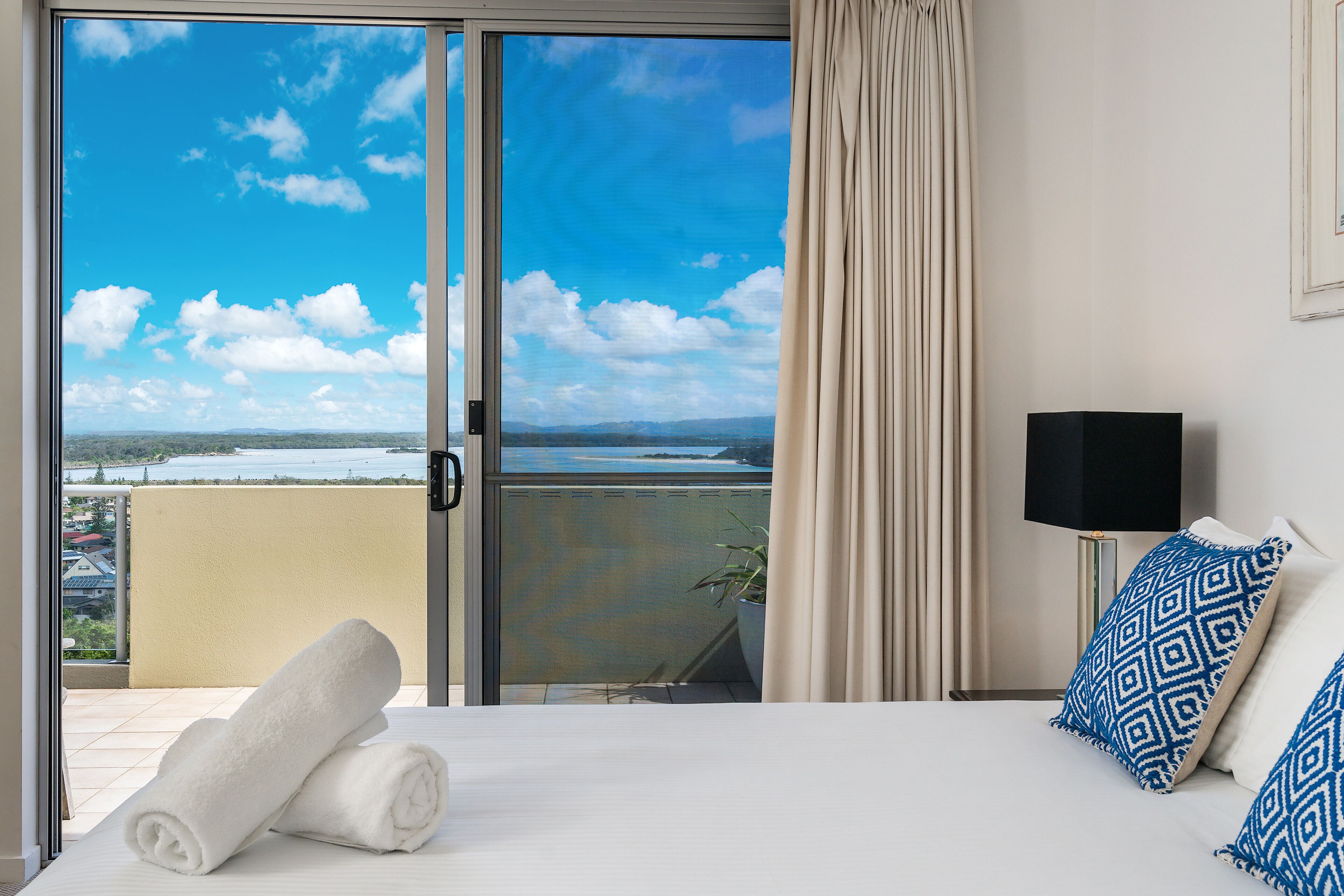 A hotel room with a bed, a TV, a view of the sea, and a balcony with a curtain.