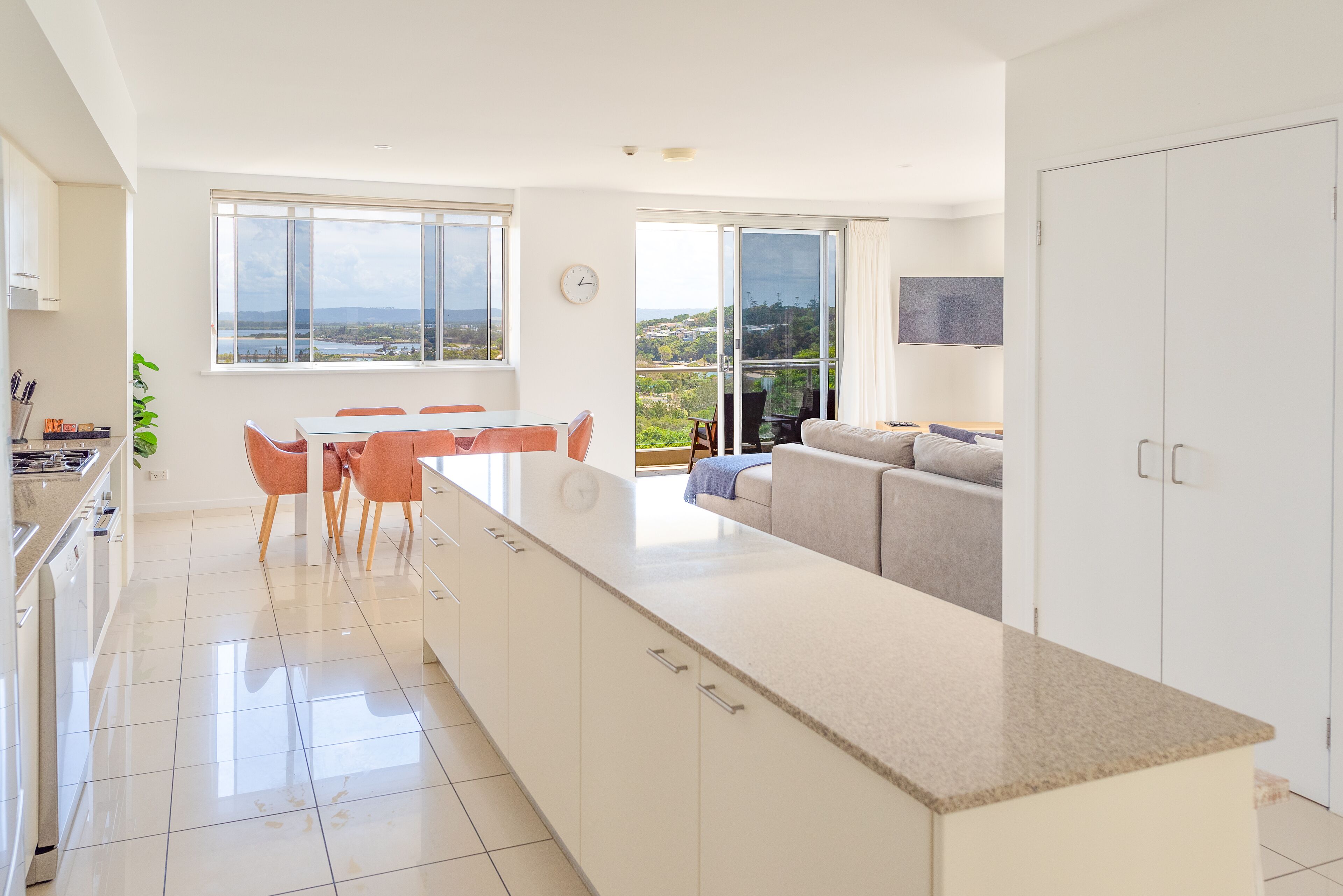 A modern kitchen with a central island, a dining area with chairs, a sofa, and a view of the outdoors.