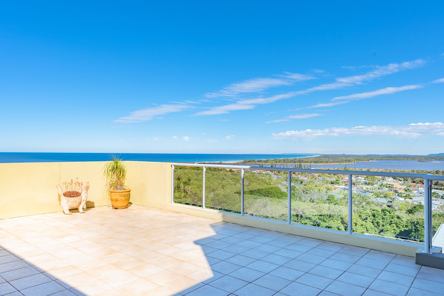 Un balcon offrant une vue sur un paysage côtier, comprenant une étendue d’eau et une ville située au loin.