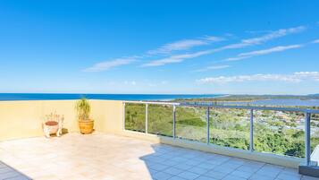 Un balcon offrant une vue sur un paysage côtier, comprenant une étendue d’eau et une ville située au loin.