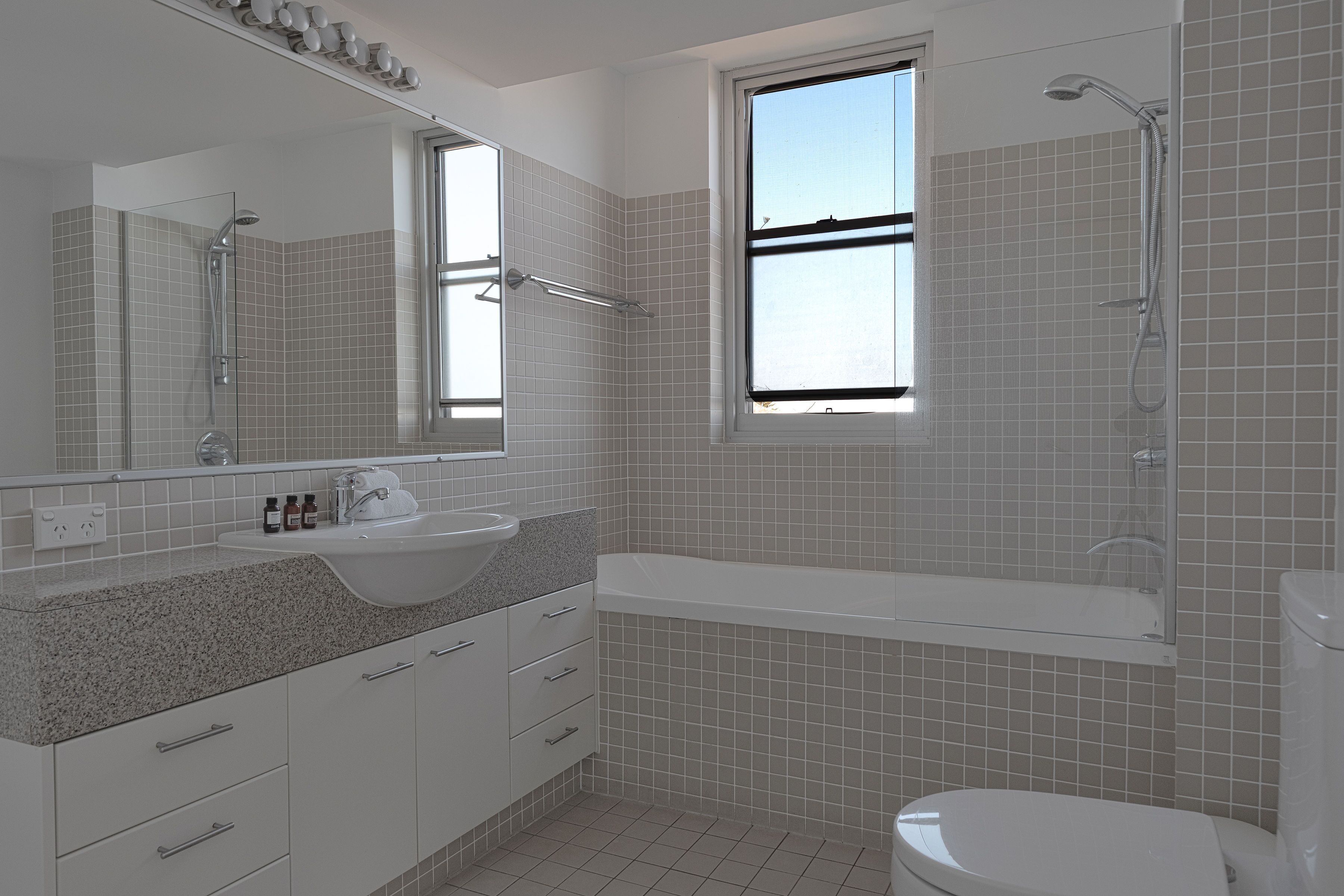 Un baño moderno con un espejo grande, un lavamanos, una ducha y un inodoro.