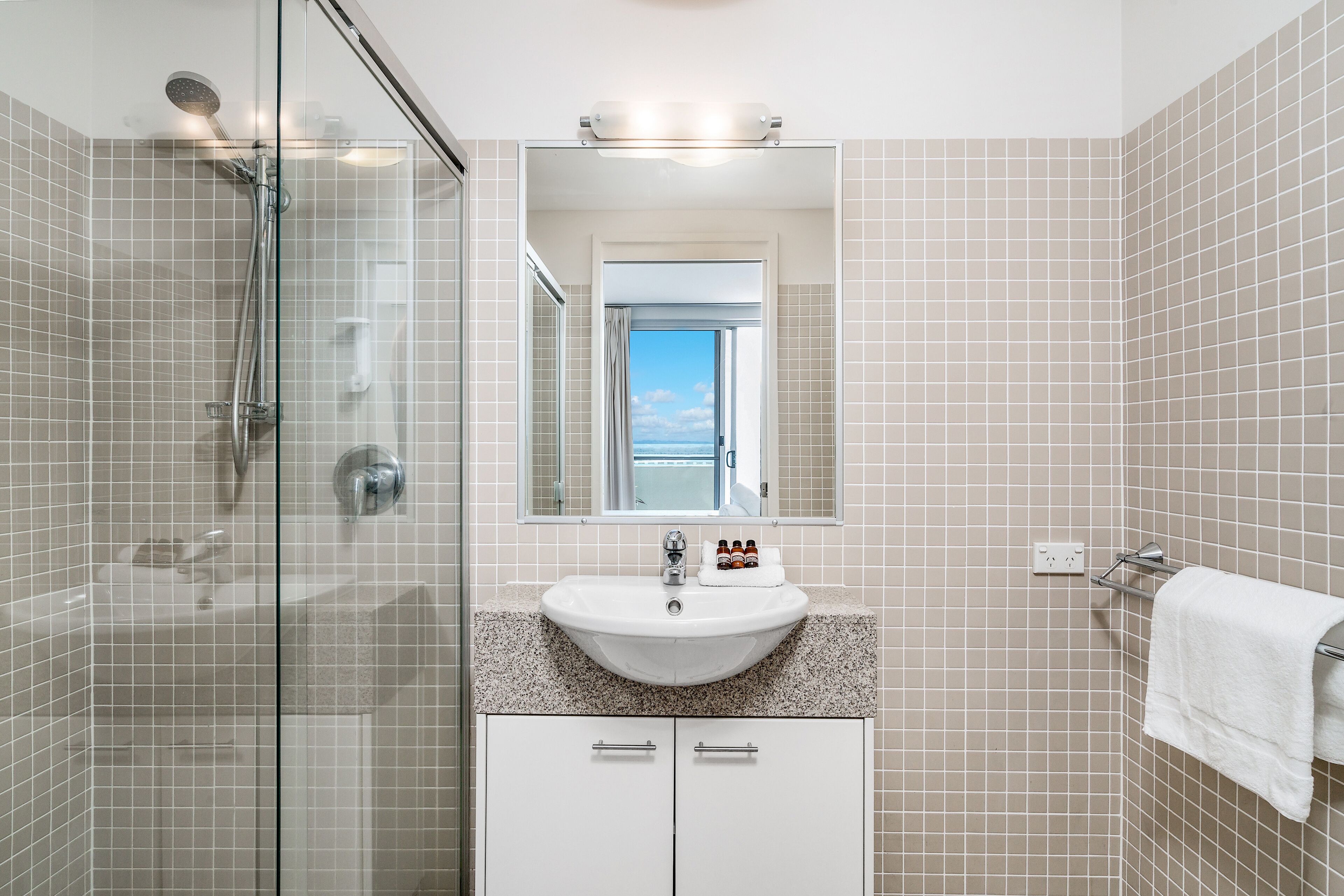 Un baño moderno con ducha de vidrio, lavamanos blanco y un espejo grande.