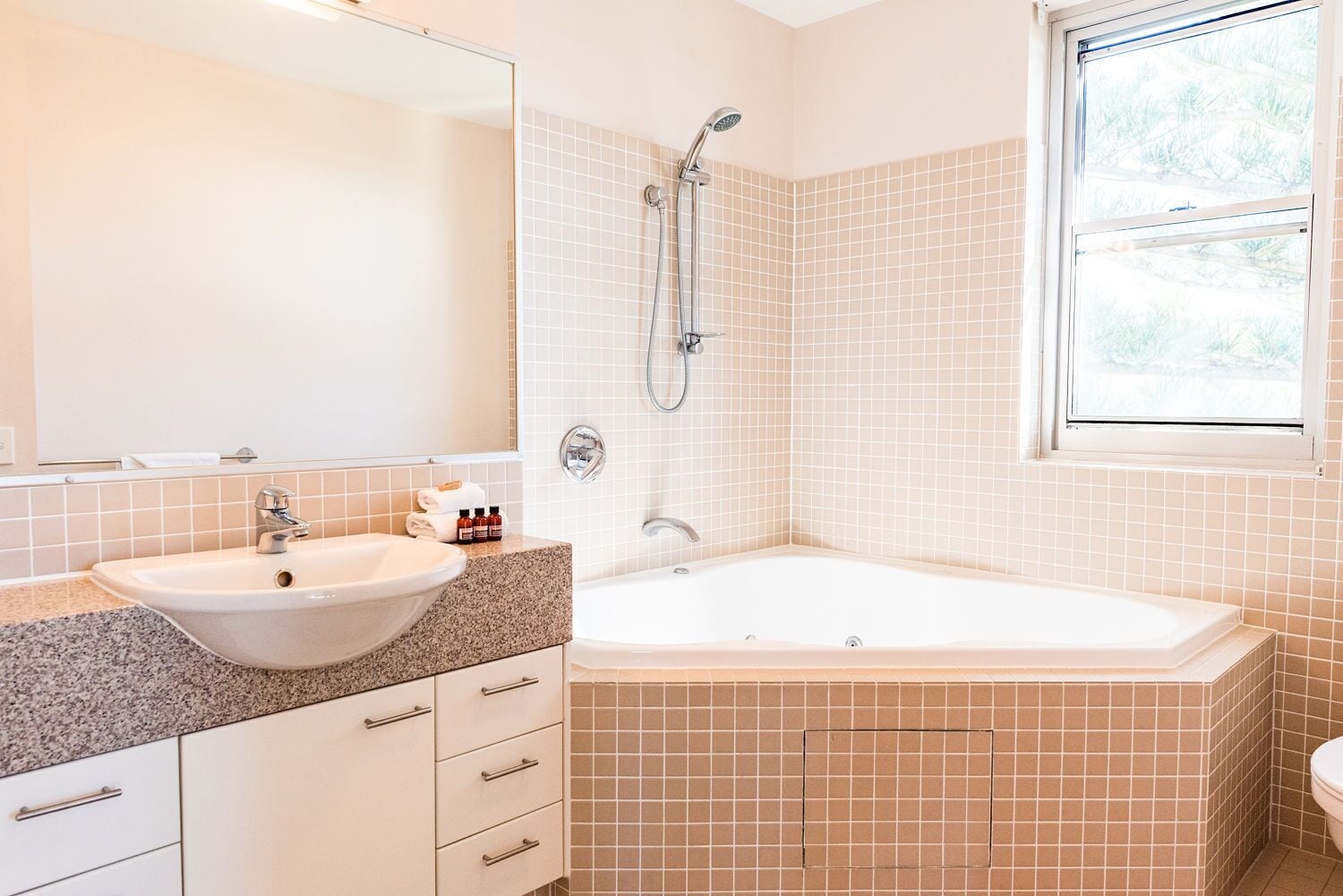 A bathroom with a sink, mirror, shower, and a window.