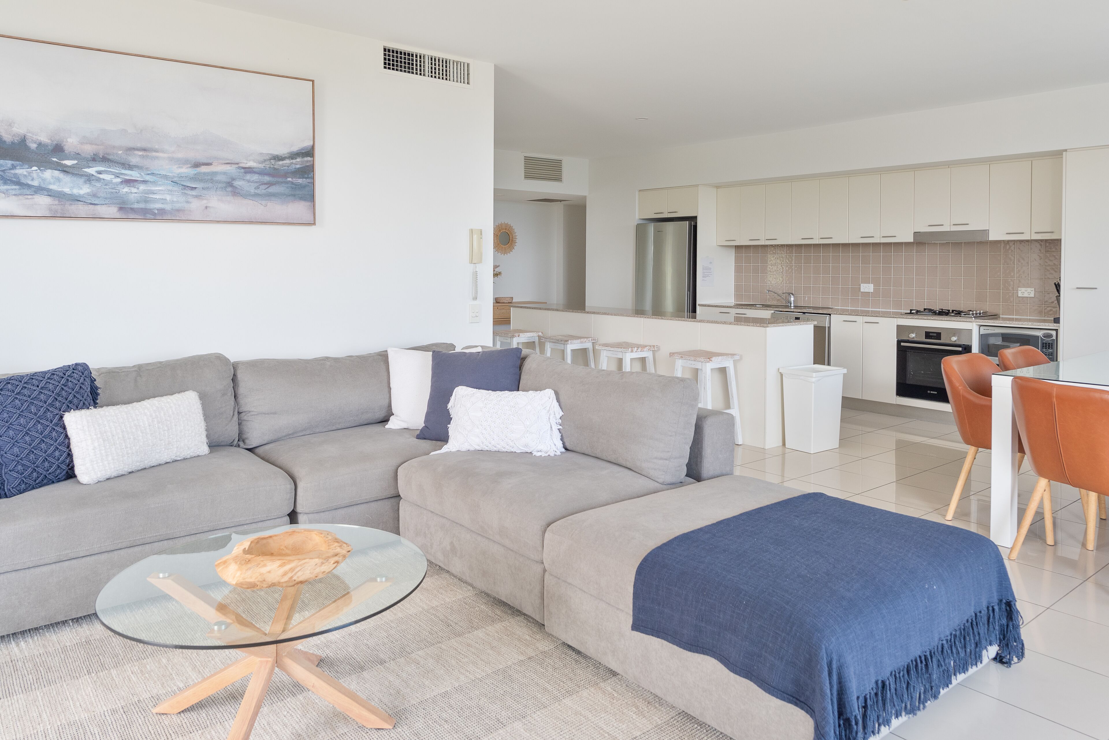Ein modernes Wohnzimmer mit einem grauen Ecksofa, einem Glastisch und einer blauen Decke.