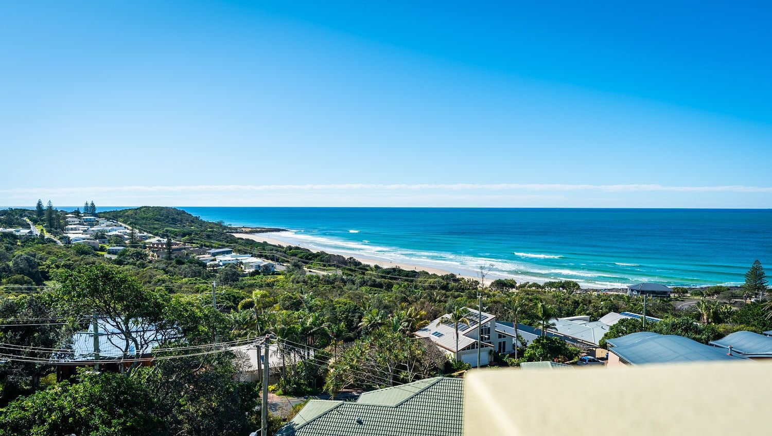 Una zona residencial costera con casas, una playa y un cielo azul despejado.