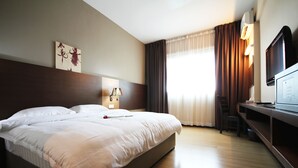 Ein Hotelzimmer mit einem großen Bett, einem Schreibtisch mit Fernseher, einer Lampe und einem Bild an der Wand.