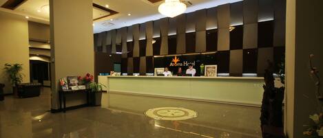 A hotel reception area with a modern design, featuring a reception desk, a chandelier, and a check-in counter.