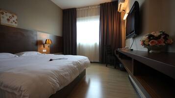 A hotel room with a large bed, a desk, a TV, and a window with curtains.