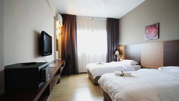 Una camera d'albergo con due letti, una televisione, una scrivania e una finestra con tende.