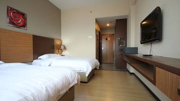 A hotel room with two beds, a TV, a desk, and a wooden headboard.