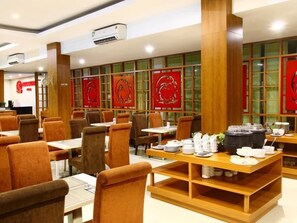 L’intérieur d’un restaurant, avec de nombreuses tables et chaises, des poutres en bois et des panneaux décoratifs rouges.