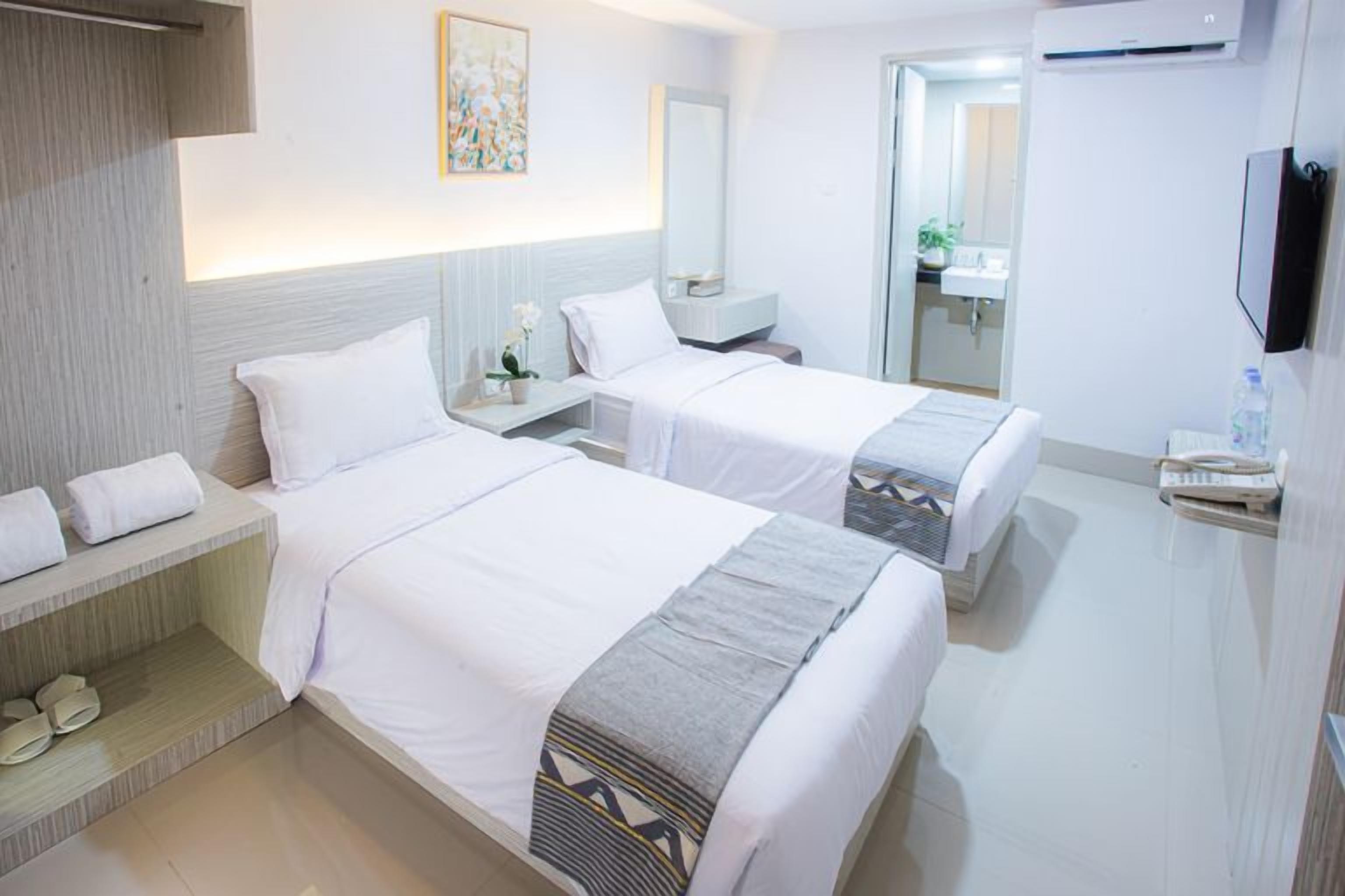 A hotel room with two beds, a bedside table, a mirror, a TV, and a bathroom visible through an open door.