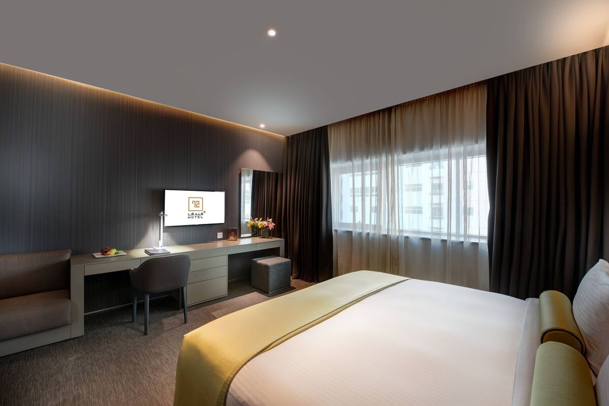 A modern hotel room with a large bed, a desk, a chair, and a TV.