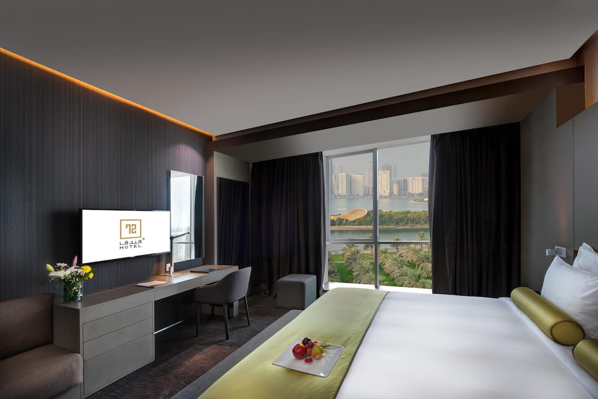 A hotel room with a bed, a desk, a TV, and a view of a cityscape.