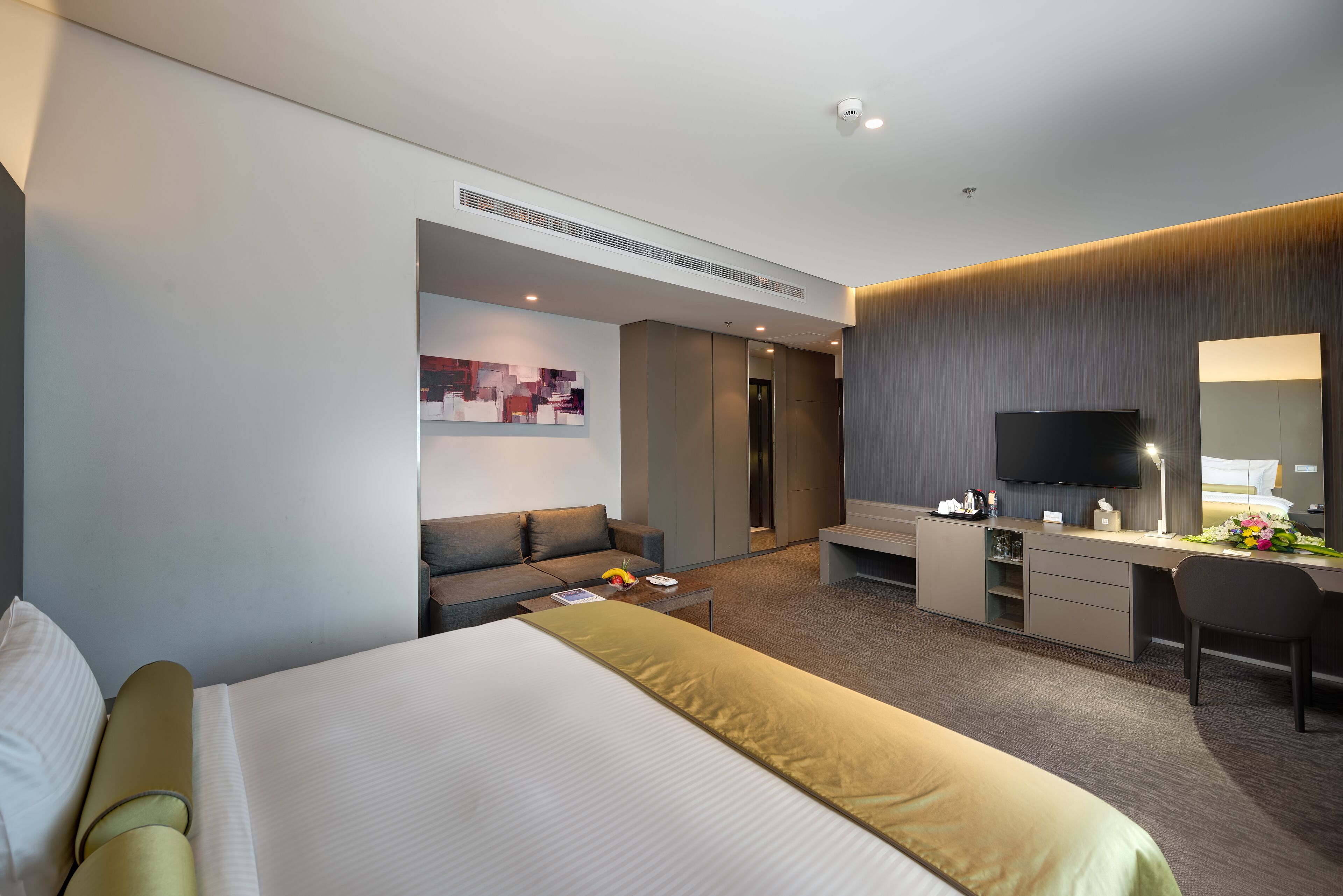 A modern hotel room with a large bed, a sofa, a desk, and a TV.