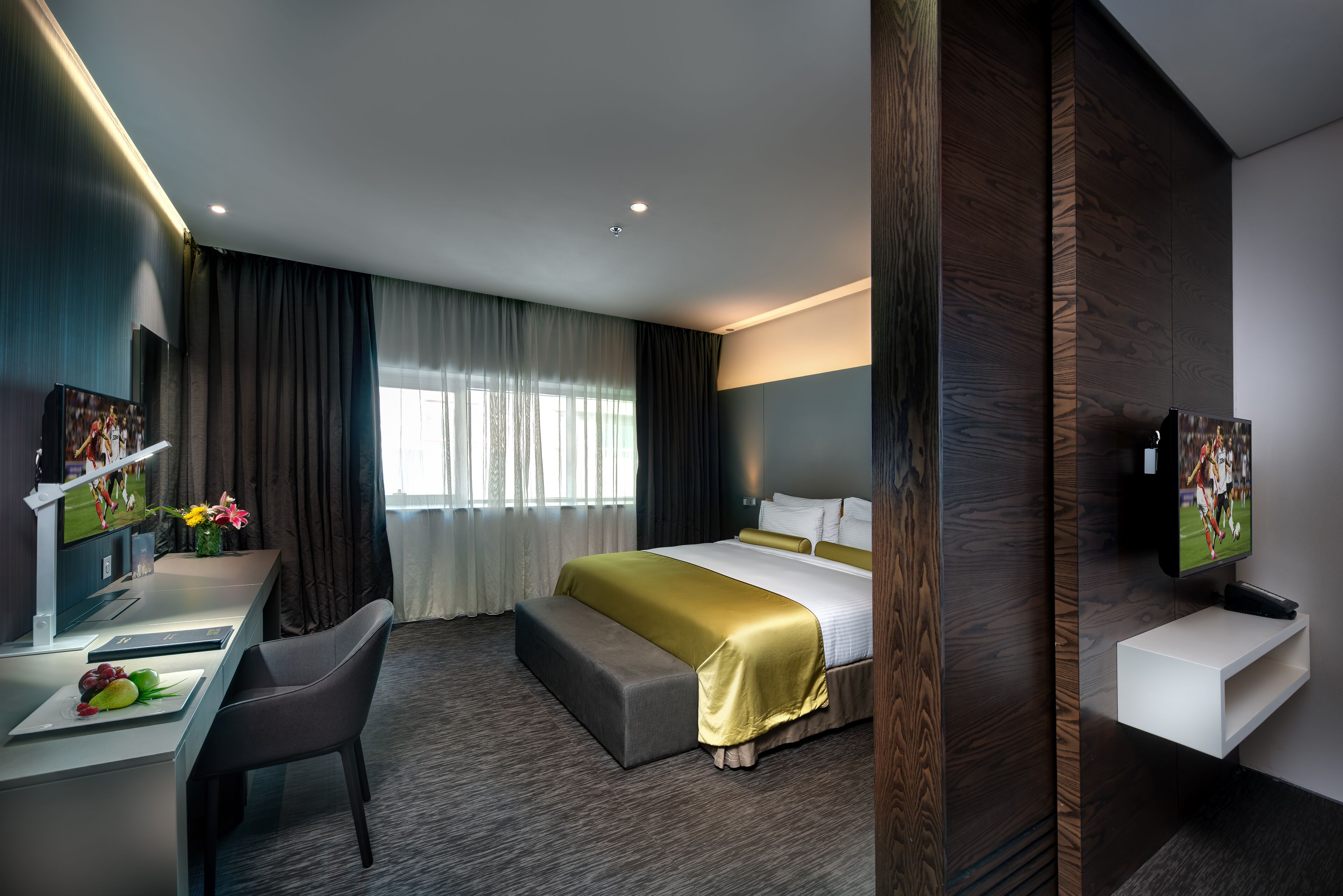 Une chambre d’hôtel moderne avec un grand lit, un bureau avec une chaise, une télévision et une petite table agrémentée d’un vase de fleurs.