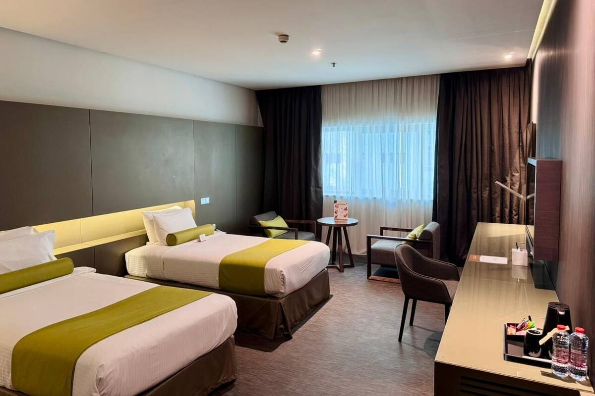 A hotel room with two beds, a desk, a chair, and a small table.