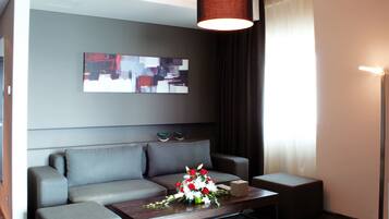 Une chambre d’hôtel moderne avec un canapé gris, une table basse en bois agrémentée d’un arrangement floral et un grand tableau abstrait accroché au mur.