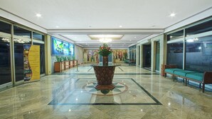 A hotel lobby with a central decorative planter, a seating area with benches, and a large informational poster on the left. - Sahid Kawanua Manado (Manado)