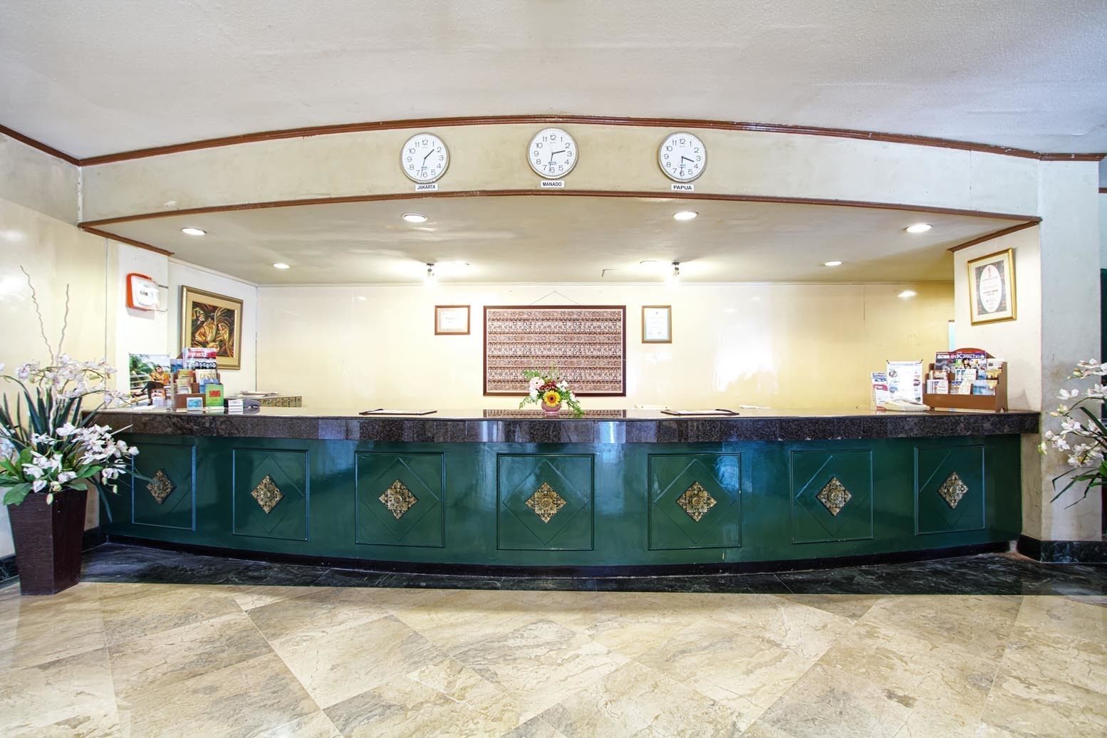 A reception area with a marble floor, a green reception desk, and three wall clocks.