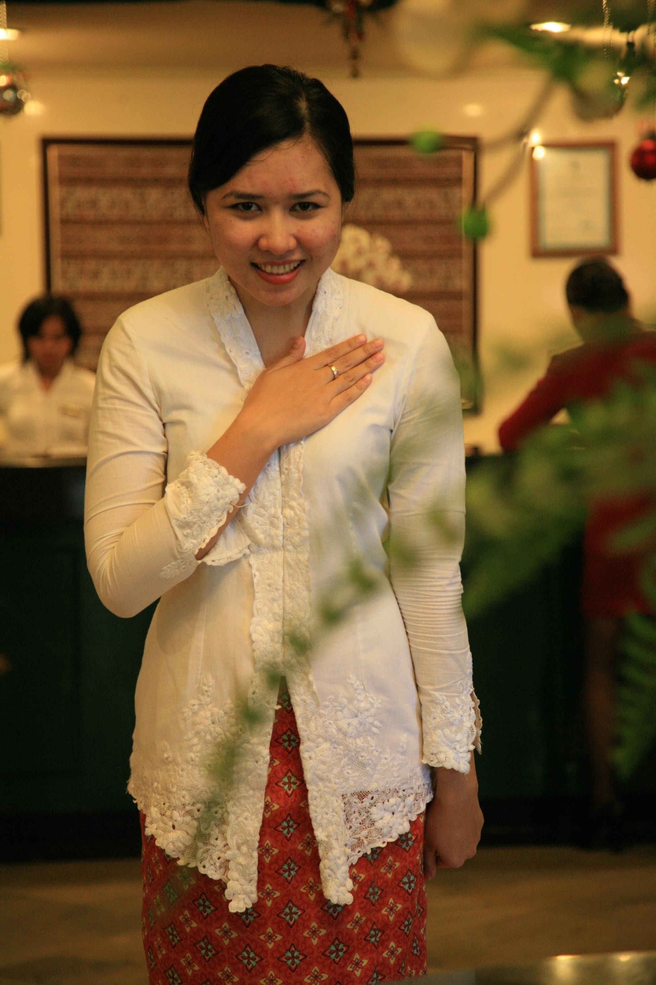 A person in a white lace blouse and red patterned skirt standing indoors.