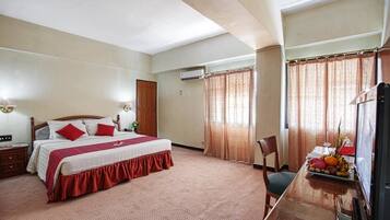 Quarto de hotel com uma cama grande, uma escrivaninha com um computador e uma cadeira.
