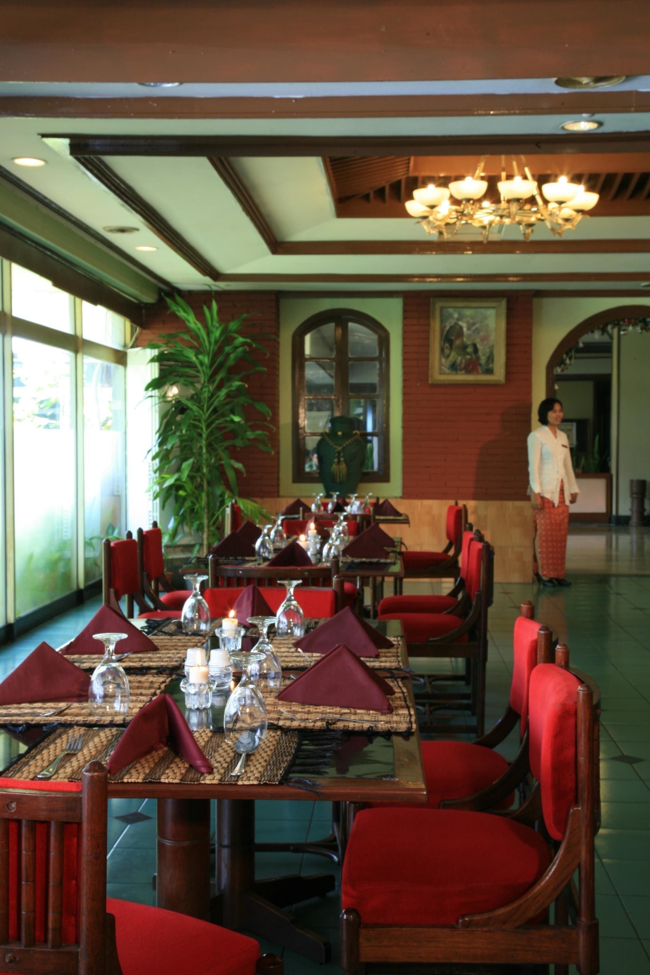 Un restaurante con sillas tapizadas en rojo y mesas dispuestas con cristalería y servilletas.