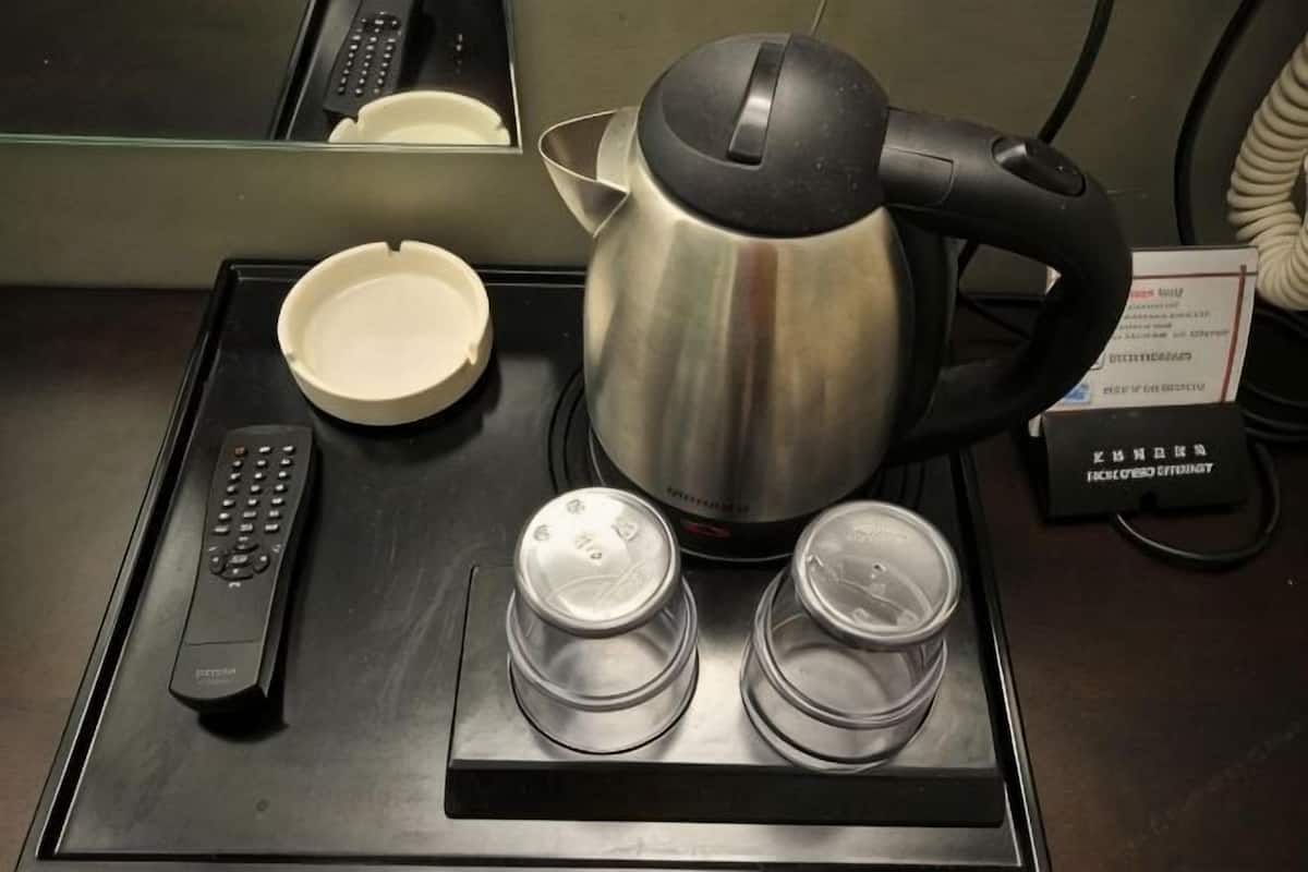 Quarto de hotel com cafeteira, controle remoto e duas xícaras em um suporte.