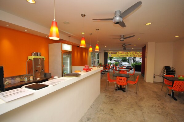 A modern restaurant interior with a white counter, orange walls, and red chairs.