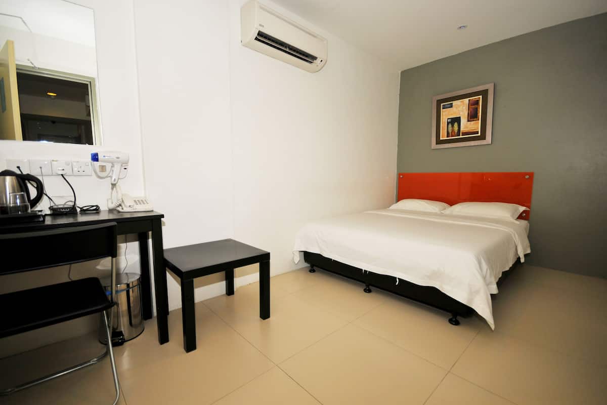 Quarto de hotel com cama, escrivaninha com cadeira, mesa pequena, aparelho de ar condicionado e quadro na parede.