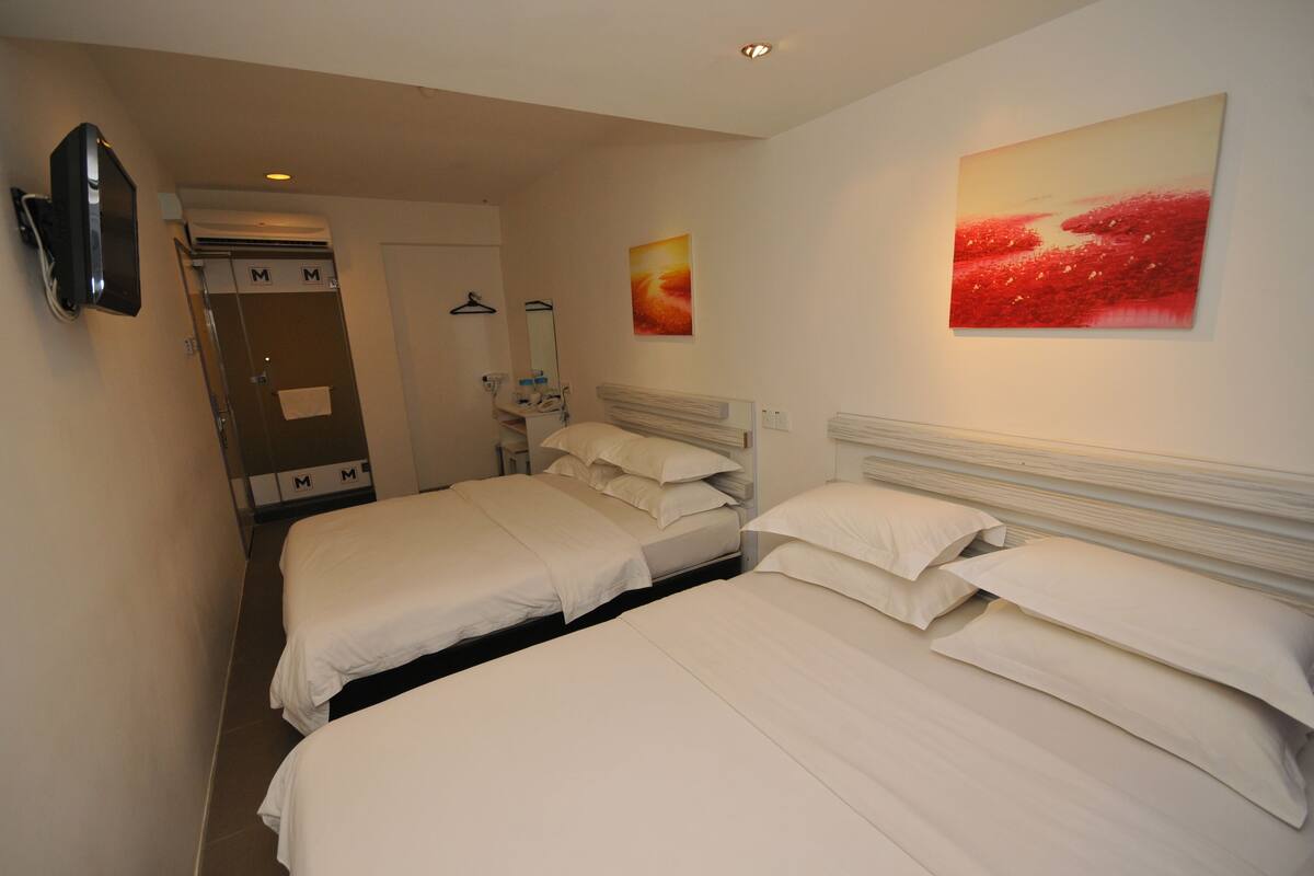 Quarto de hotel com duas camas, banheiro com chuveiro e televisão fixada na parede.
