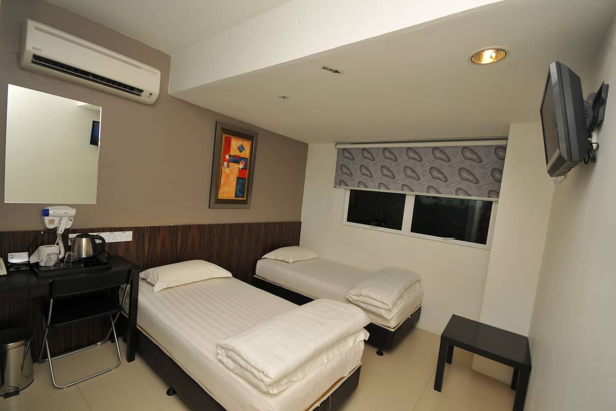 Quarto de hotel com duas camas, uma escrivaninha com chaleira, espelho, ar condicionado, televisão e janela com persiana estampada.