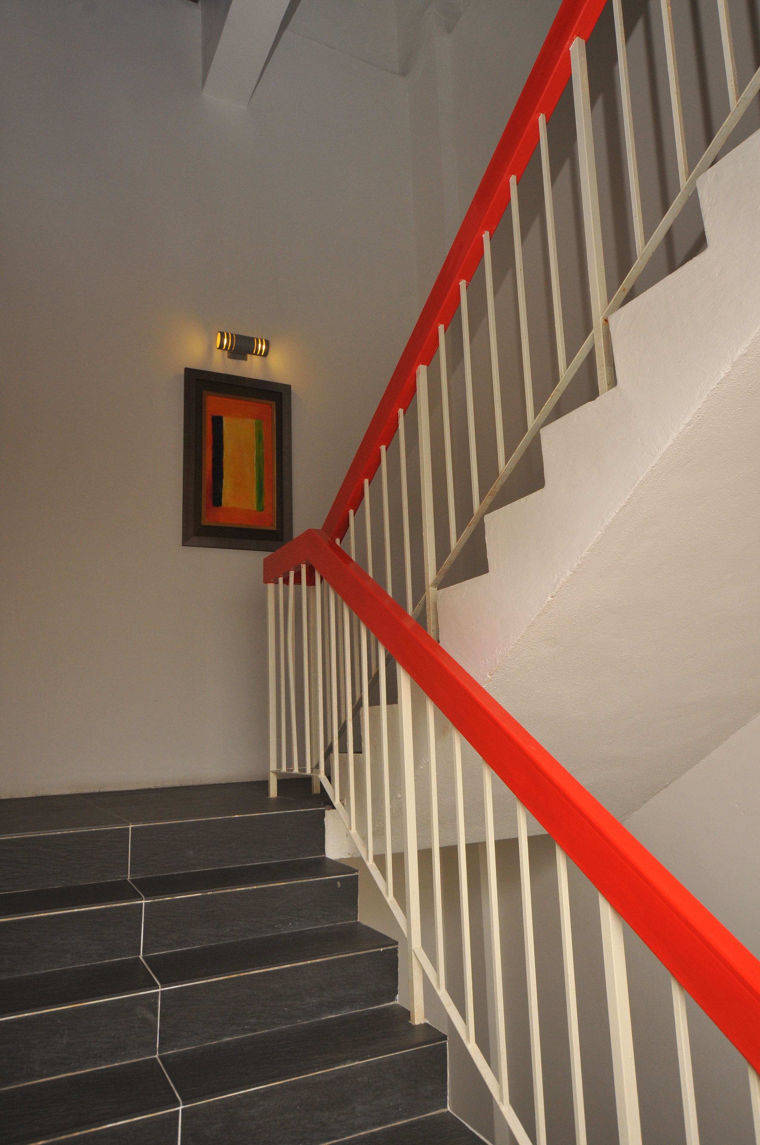 A staircase with black steps and a red handrail, leading to a landing with a framed artwork.
