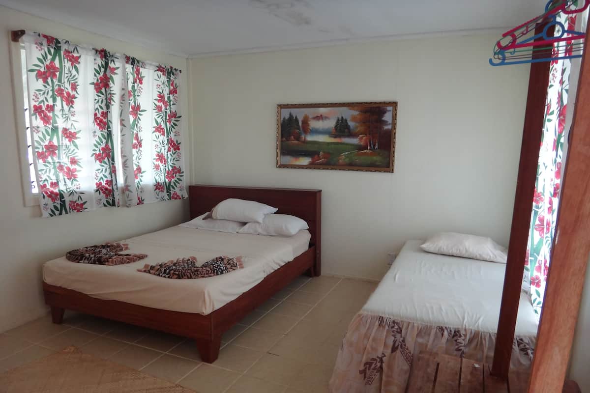 A bedroom with two beds, floral curtains, a painting, and a tiled floor.