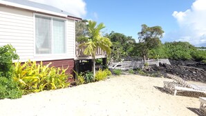 Una propiedad frente a la playa con un edificio blanco, una terraza de madera y una zona arenosa con cercado de madera.