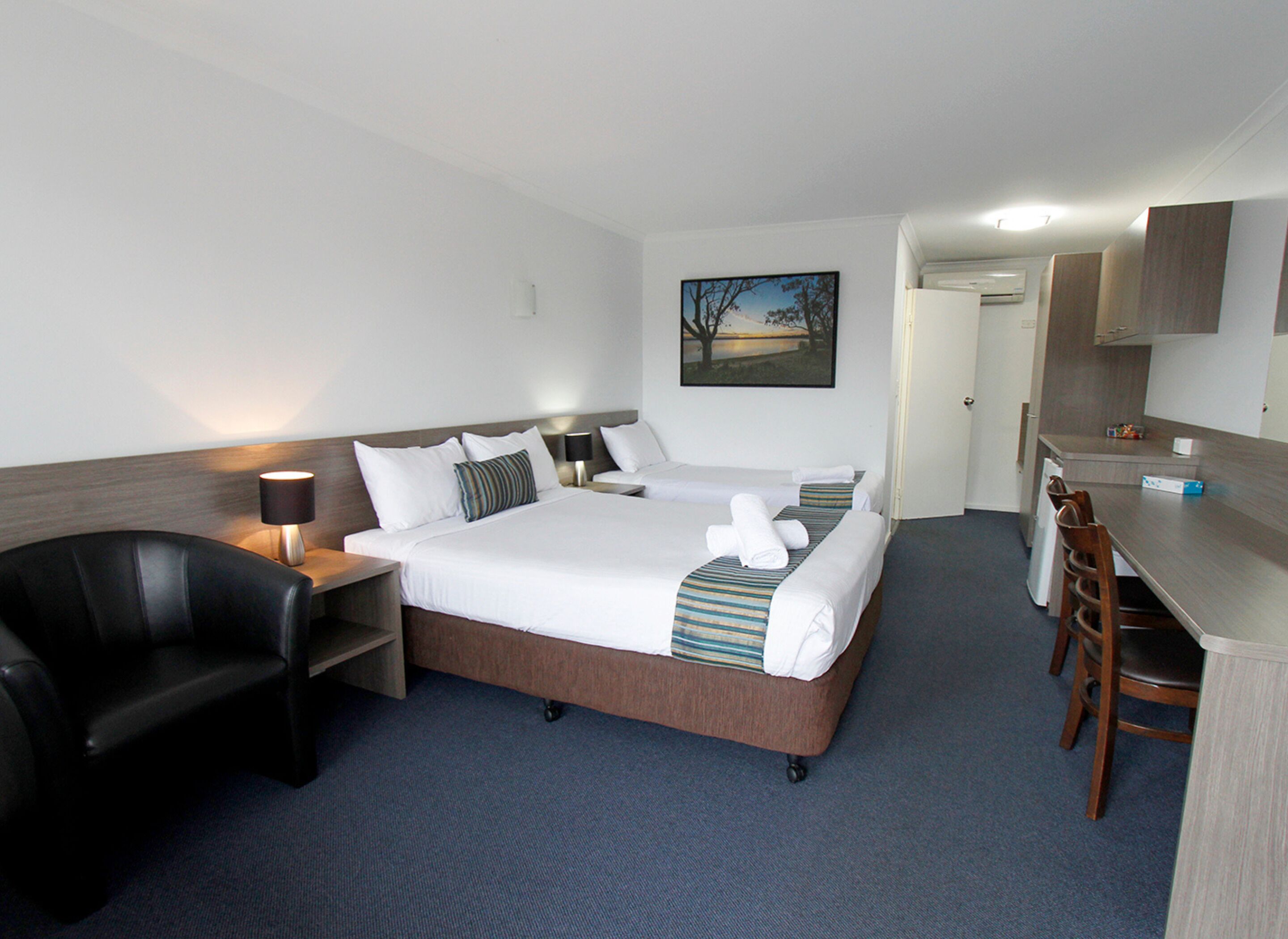 Een hotelkamer met twee bedden, een bureau, een stoel, een lamp en een schilderij aan de muur.