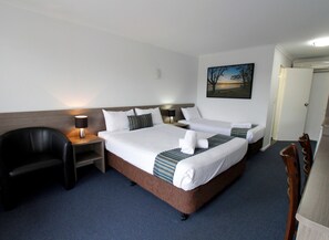 A hotel room with two beds, a desk, a chair, and a painting on the wall.
