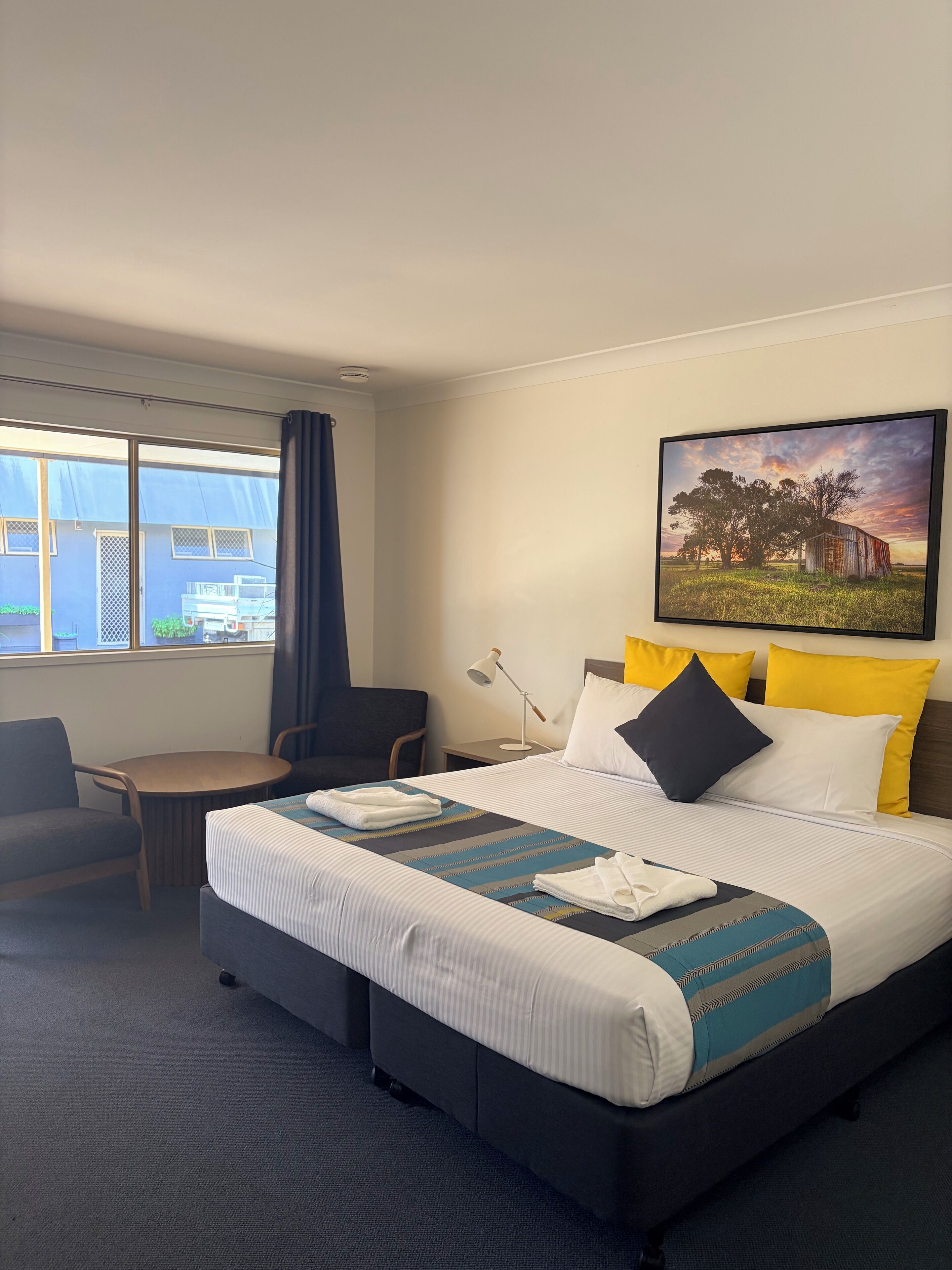 A hotel room with a large bed, a desk, a chair, and a window with curtains.