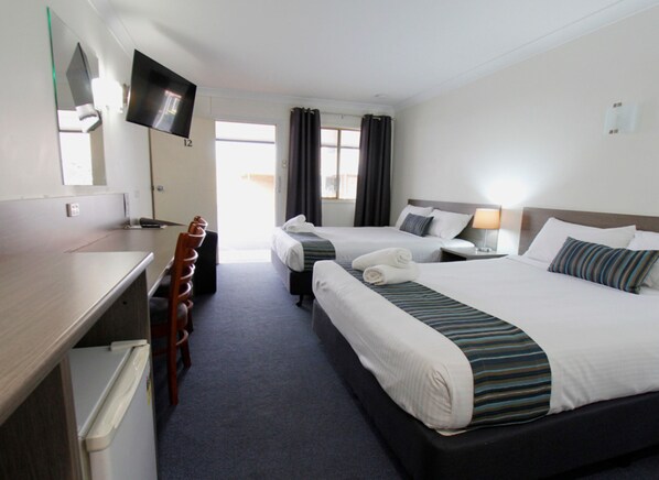 A hotel room with two beds, a desk, a chair, a TV, and a window with curtains.
