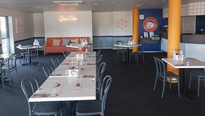 Ein Restaurant mit mehreren Tischen und Stühlen, einem Neonlichtschild mit der Aufschrift "Good Times" und einer Wand mit dem Logo "Buddy Boy Kitchen".